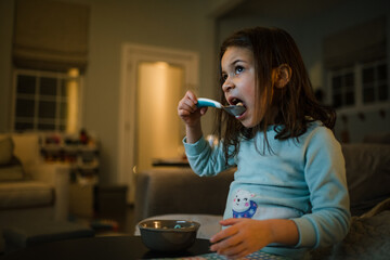 Girl eating cereal in front of tv in the early morning