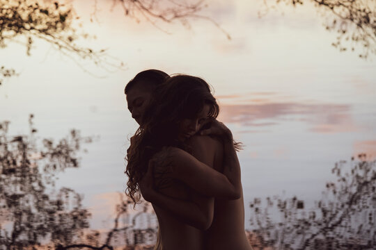 pretty lesbian queer couple share intimate hug by pastel lake water