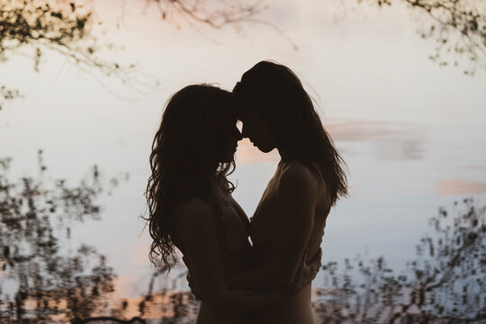 romantic pastel coloured silhouette of lesbian queer couple by lake