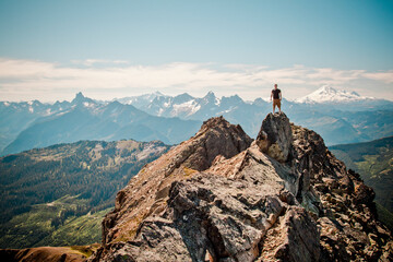 Hiker stands on summit of mountain with scenic view behind.