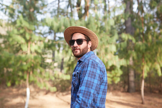 young man with beard and hat looking at camera in the forrest