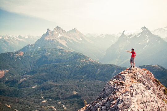 Hiker pointing across valley from rocky mountain summit