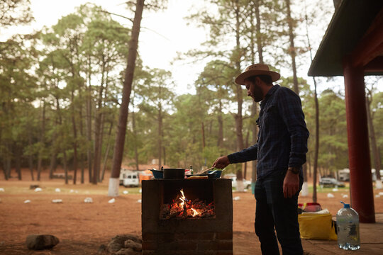 young man preparing dinner at the campfire next to his campsite