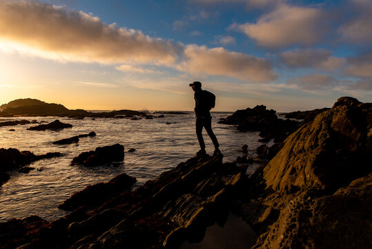 Silhouetted figure standing on shore with dramatic sunset in sky