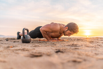 muscular hispanic man performing push-ups on the beach during sunrise
