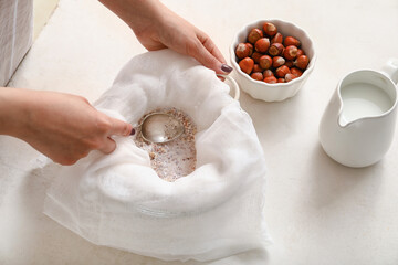Woman preparing tasty hazelnut milk on kitchen table, closeup