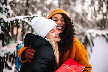 Happy girlfriends embracing holding Christmas gift by Christmas tree