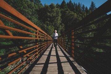 Teen Boy Stands at the End of a Rust Colored Bridge in the Early Eve