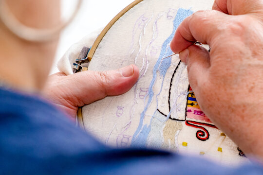 Close-up of the hands of an elderly woman embroidering on a fabric. Tr