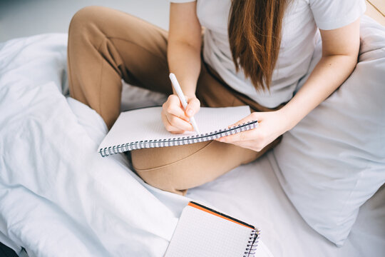 girl writes in a notebook and listens to music in bed