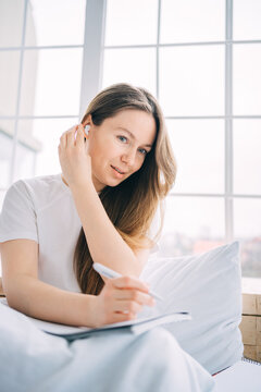 girl writes in a notebook and listens to music in bed
