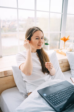 girl works at a laptop and listens to music in bed