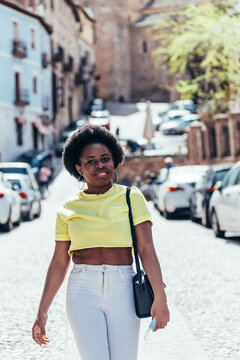 Black girl with afro hair walking happily down a city street.