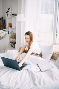 girl writes in a notebook and listens to music in bed