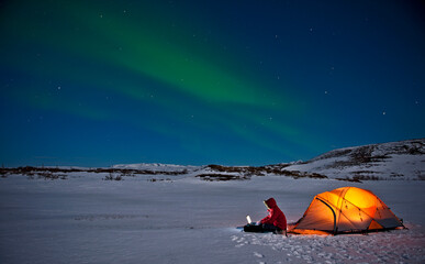 Scientist sits outside of her tent with Northern Lights in the sky