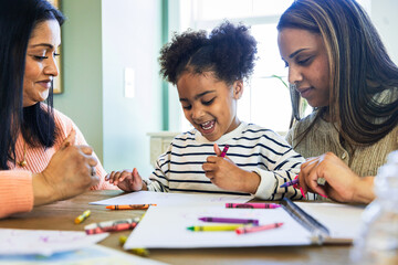 Mother and grandmother with cheerful girl drawing with crayon on paper at home