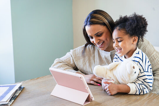 Smiling daughter and mother using digital tablet at home