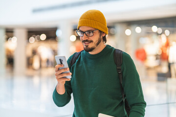 Modern spanish man smiling and using smartphone in shopping mall