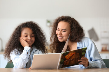 African-American little girl with her mother reading book at home