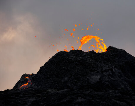 Orange lava over carter of erupting volcano at sunset