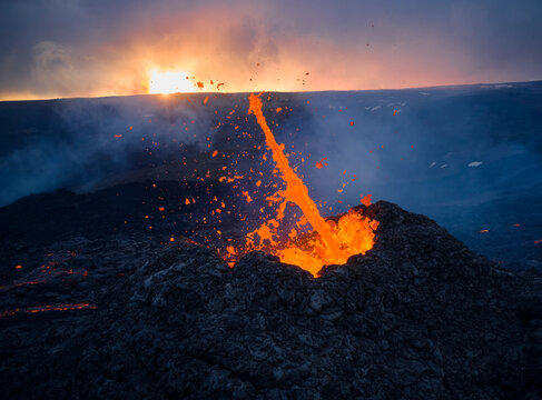 Burning hot lava splashing in volcano crater in overcast evening
