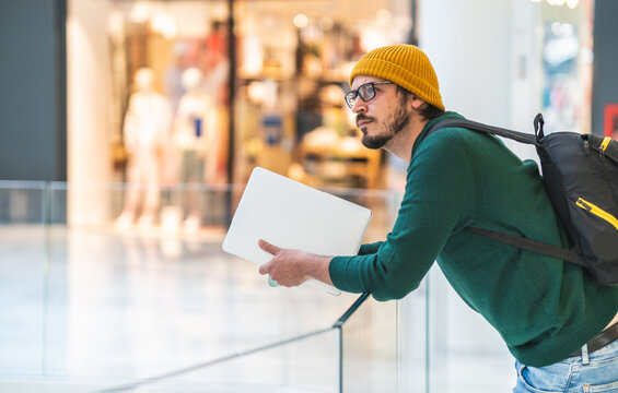 Modern spanish man with glasses and laptop posing in shopping mall