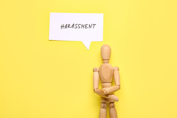 Paper with word HARASSMENT and wooden mannequin on color background