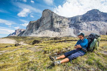 Backpacker resting, sitting in grassy meadow below mountain summit.
