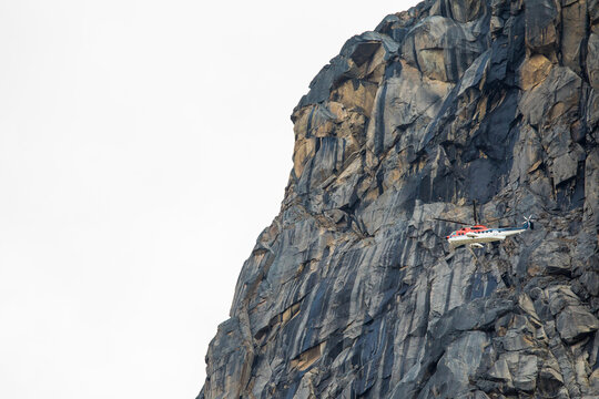 Helicopter flies next to mountain cliff.
