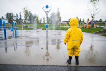 Toddler in rain suit and boots looks at the water park on a wet day