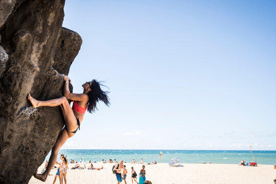 Brunette woman in bikini climbing a rock at the beach on a sunny day