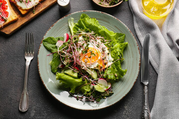 Plate of tasty salad with vegetables, fried egg and micro green on dark background
