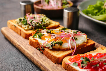 Wooden board with delicious toasts on dark background, closeup
