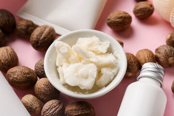 Bowl of shea butter, nuts and cosmetic products on color background, closeup