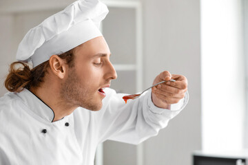 Handsome chef testing sauce in kitchen, closeup