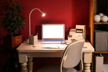 Modern workplace with computer and glowing lamp near color wall
