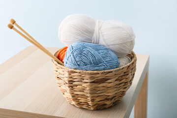 Basket with knitting yarn and needles on table against color background