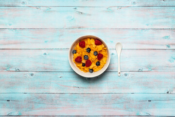 Bowl of cereal with blueberries and raspberries on blue wood