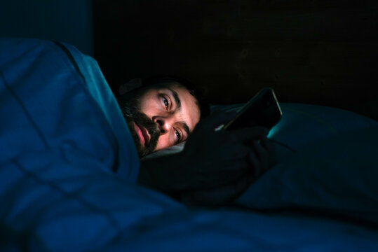 Young man lying in bed and using mobile phone