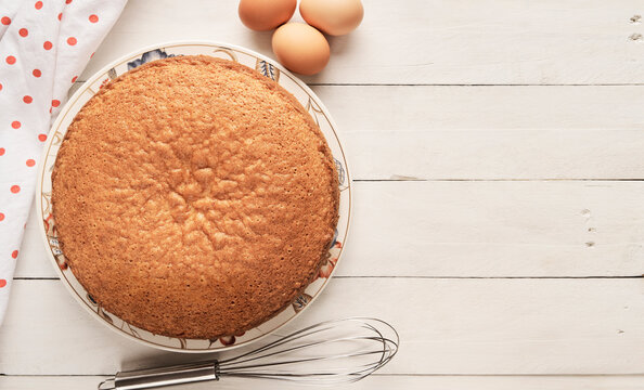 Top view of a homemade sponge cake and eggs on a white wooden table