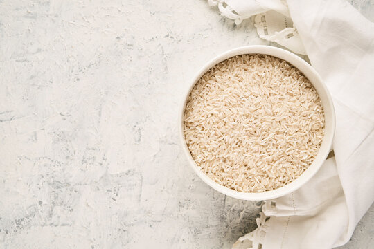 Top view of a bowl filled with raw white rice on a textured background