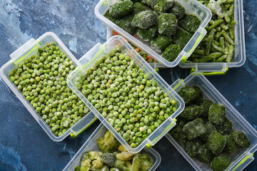 Plastic containers with different frozen vegetables on color background
