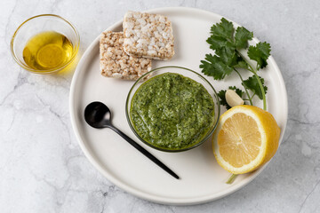 Green homemade sauce with cilantro, lemon and garlic on the white plate. Cilantro pesto. Top view. Healthy eating concept.
