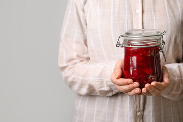Woman holding glass jar with sweet cherry jam on grey background, closeup
