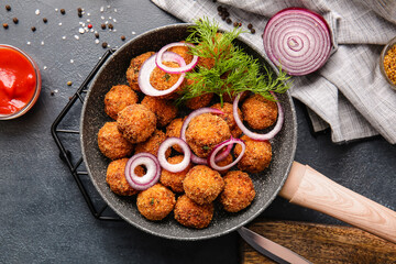 Frying pan with tasty cod cutlets and sauce on dark background