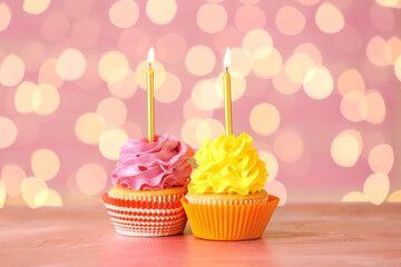 Tasty Birthday cupcakes with burning candles on table against blurred lights