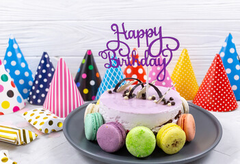 Violet birthday cake with topper Happy birthday, paper hats, macaroons on a table. Decoration for...