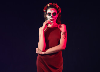Young woman with painted skull on her face against dark background. Celebration of Mexico's Day of the Dead (El Dia de Muertos)