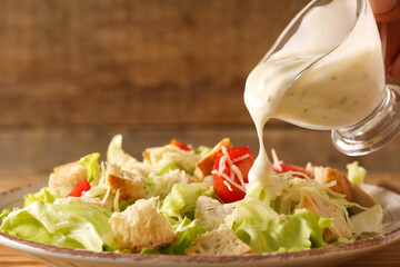 Adding sauce onto plate with tasty Caesar salad on wooden background, closeup - obrazy, fototapety, plakaty