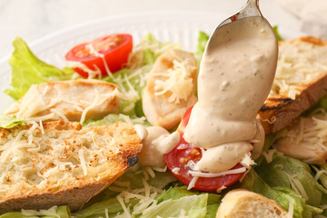 Adding sauce onto plate with tasty Caesar salad on table, closeup
